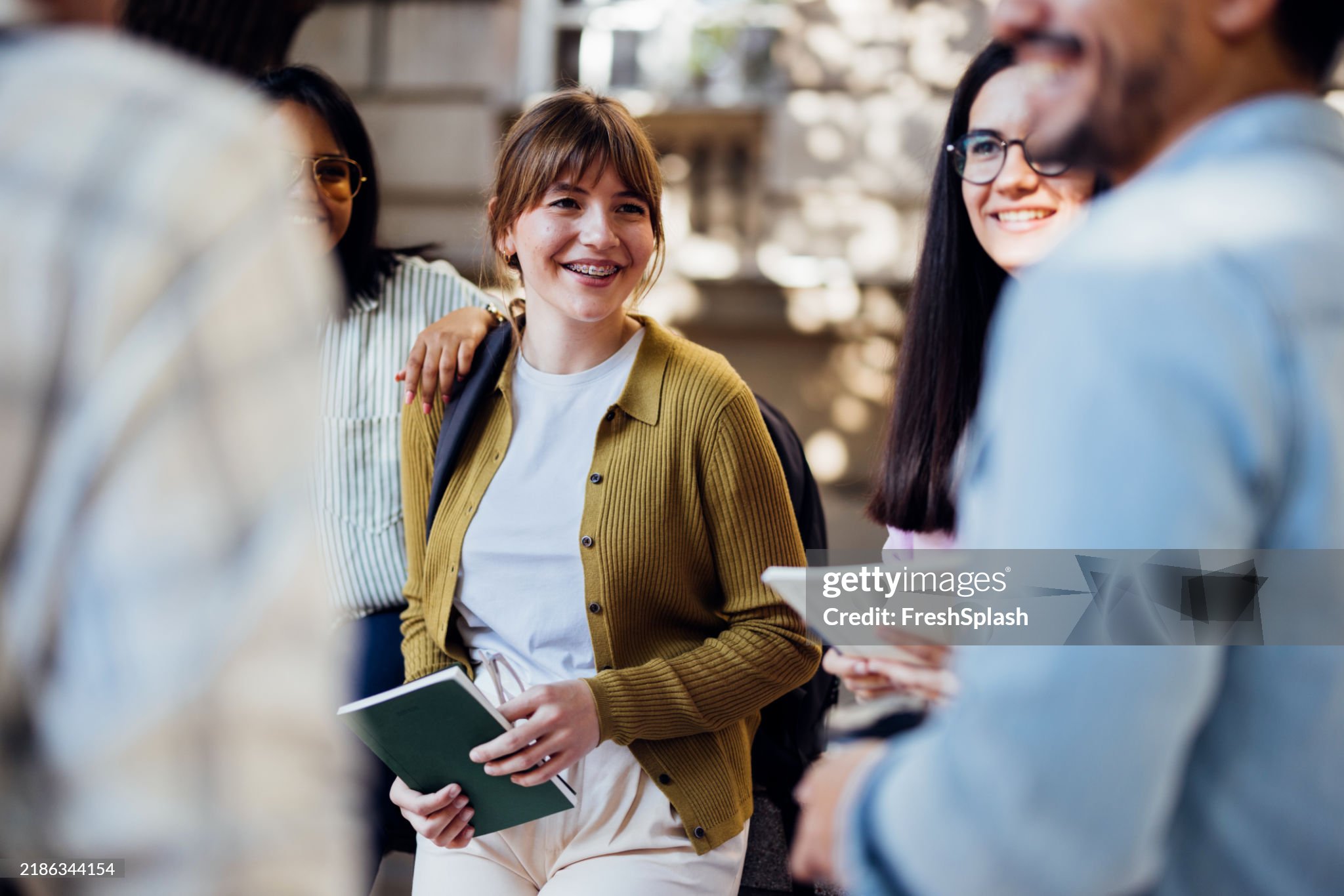 A group of cheerful young students gather outside, engaging in conversation and laughter on a sunny day. They exude joy and camaraderie, creating a positive atmosphere.